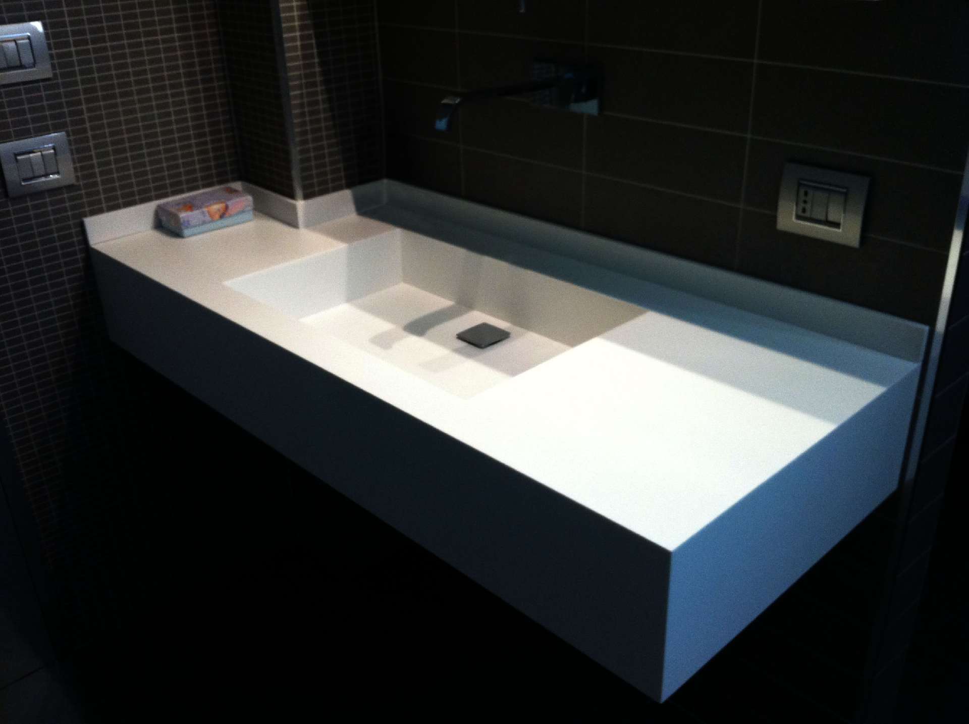 Lavabo in Corian bianco su parete a mosaico scuro